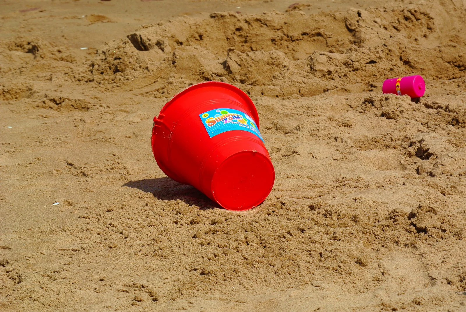 An overturned red plastic beach bucket on sand — a softer kind of bucket than the one you're about to wrangle.