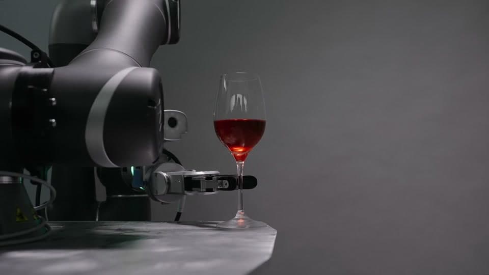 Raw camera frame of a robot gripper beside a wine glass